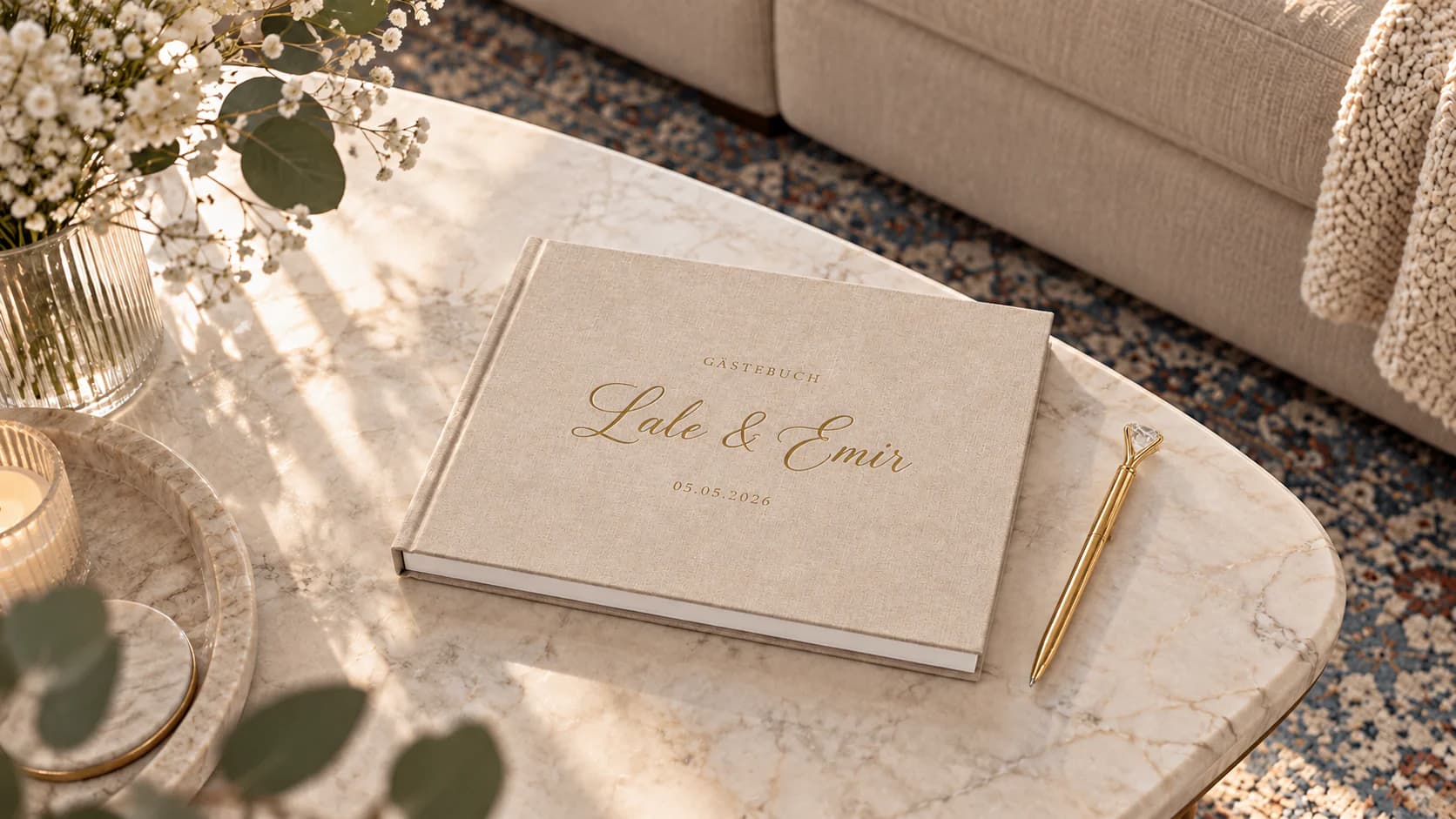 A beige landscape guest book with gold names and date on a marble table beside a gold pen.